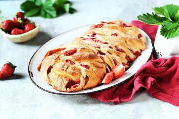 Yeast babka with strawberries and sugar in a dish on a gray background