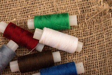 Several coils of multicolored sewing thread against a background of coarse-textured burlap. Close up.