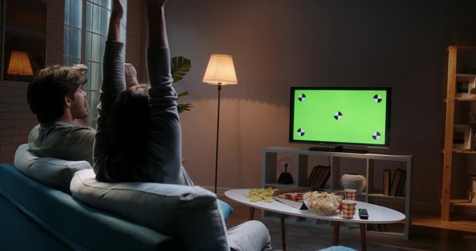 Emotional sports fan couple spending time together watching chroma-key green screen tv and reacting to their team play. 4k footage template