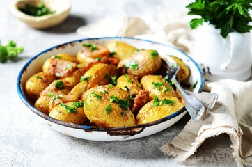 Young baked potato with bacon, spices and herbs in a baking dish on a gray background, still life