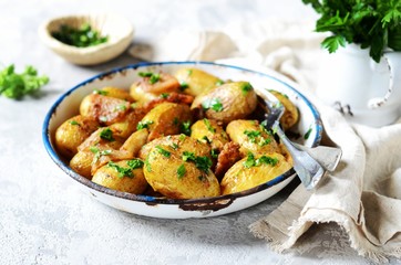 Young baked potato with bacon, spices and herbs in a baking dish on a gray background, still life