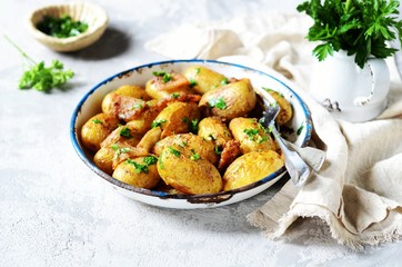 Young baked potato with bacon, spices and herbs in a baking dish on a gray background, still life