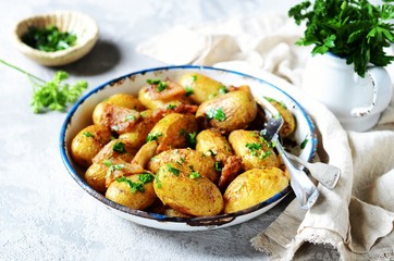Young baked potato with bacon, spices and herbs in a baking dish on a gray background, still life