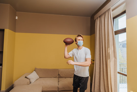man in medical mask holding american football in living room