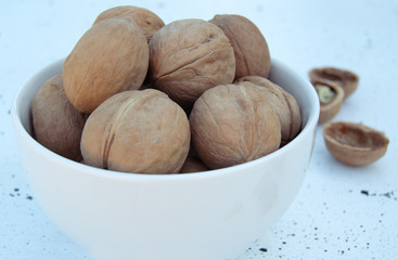 Walnuts in a shell in a white bowl on a white background. Close up.