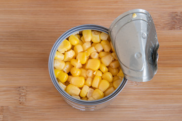 Open can of fresh sweet corn on wooden board. Focus on corn. Tin filled with cooked maize.