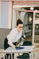 Waitress disinfecting restaurant chairs and tables before the next customers sit down. New normal