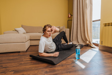 tired man lying on fitness mat near sports bottle with water, end of quarantine concept