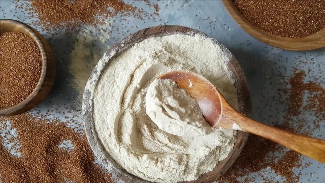 Teff flour in a bowl with a spoon and teff grain top view