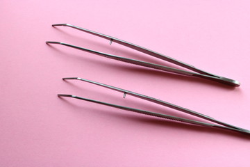 two metal tweezers on a pink background