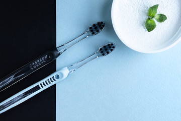 Toothbrushes and tooth powder on a blue-black background with mint leaves. Flat lay.