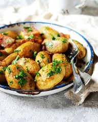 Young baked potato with bacon, spices and herbs in a baking dish on a gray background, still life