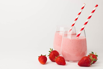 Glass of fresh strawberry milkshake, smoothie and fresh strawberries on pink, white and wooden background. Healthy food and drink concept.