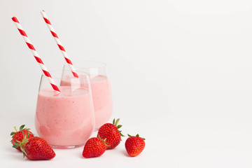 Glass of fresh strawberry milkshake, smoothie and fresh strawberries on pink, white and wooden background. Healthy food and drink concept.