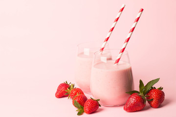 Glass of fresh strawberry milkshake, smoothie and fresh strawberries on pink, white and wooden background. Healthy food and drink concept.