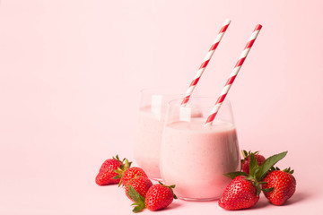 Glass of fresh strawberry milkshake, smoothie and fresh strawberries on pink, white and wooden background. Healthy food and drink concept.
