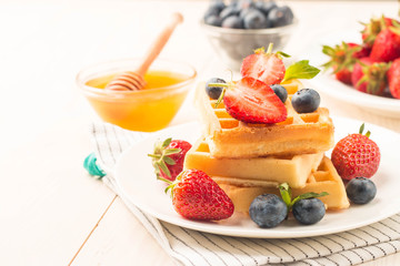 Fresh homemade food of berry Belgian waffles with honey, chocolate, strawberry, blueberry, maple syrup and cream. Healthy dessert breakfast concept with juice