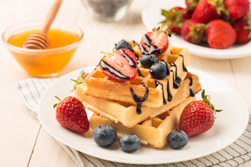 Fresh homemade food of berry Belgian waffles with honey, chocolate, strawberry, blueberry, maple syrup and cream. Healthy dessert breakfast concept with juice