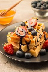 Fresh homemade food of berry Belgian waffles with honey, chocolate, strawberry, blueberry, maple syrup and cream. Healthy dessert breakfast concept with juice