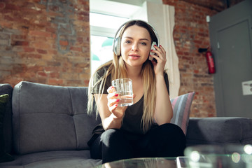 Young woman wearing wireless headphones gesturing during a video conference in the living room. Communication during insulation, pandemic, remote working or meeting with friends, family. Devices, tech