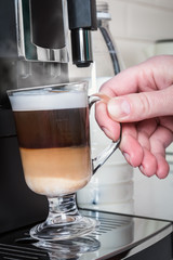 hand picks up a glass of hot cappuccino made in the coffee machine