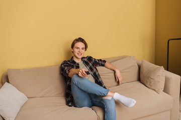 Obraz premium happy man holding remote controller and sitting on sofa, end of quarantine concept