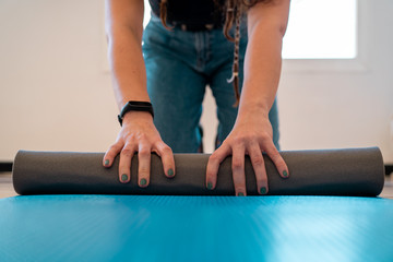 A woman on jeans and wearing a sports band rolling up a violet yoga mat on the floor in her apartment after an active sports session at home