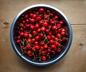Iron bowl filled with ripe homemade sweet cherry wooden background
