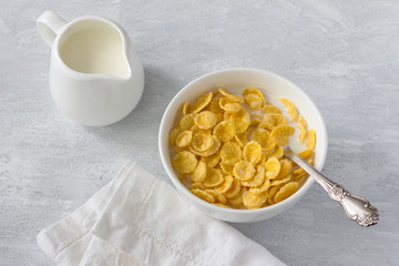 Sweet crunchy cornflakes with milk on a gray textured background. Fast tasty breakfast, top view, horizontal	