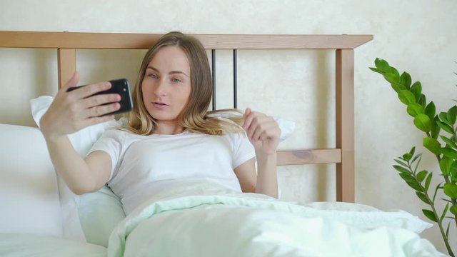 Smiling Woman is Making a Video Call with a Smartphone Just Woke up in a Cosy Bed in a Bedroom in the Morning.
