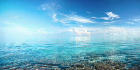 Obraz premium Beautiful seascape with blue sky and white clouds over transparent clear turquoise ocean water and picturesque stones in foreground.