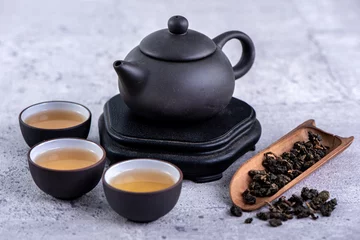 Foto op Aluminium Hot tea in black teapot and cups and dry tea leaves over bright gray cement background, close up, copy space design concept. © RomixImage