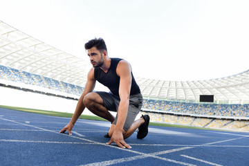 handsome runner in start position on running track at stadium