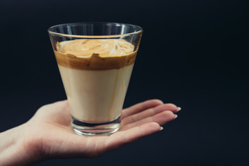 Glass of trendy Korean Dalgona coffee in the palm of hand on a black background