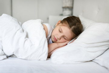 Obraz na płótnie Canvas Tired Caucasian girl child sleeps with a phone on a white pillow, top view, the concept of children and gadgets, child health and child safety online