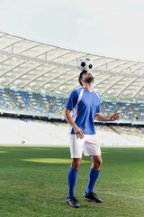 professional soccer player in blue and white uniform with ball on head at stadium