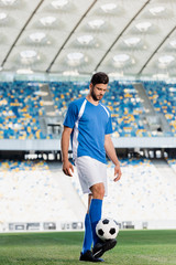 professional soccer player in blue and white uniform with ball on football pitch at stadium