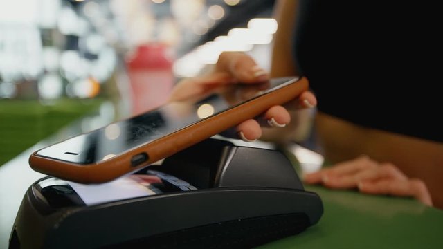 Mobile NFC payment for order in gym cafe. Hand of woman customer paying through mobile phone over pos terminal. money transfer through smartphone app. Apple pay concept