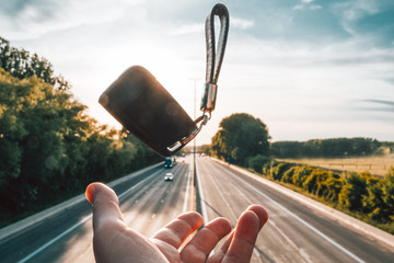 close up on hand catching car key floating on the air above the highway on sunset - travel, road lifestyle concept
