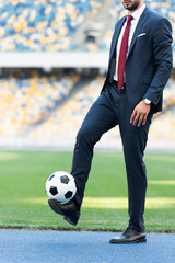 cropped view of young businessman in suit playing with soccer ball at stadium