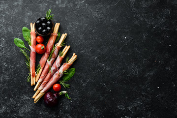 Prosciutto ham and grissini bread sticks. On a black stone background. Top view.