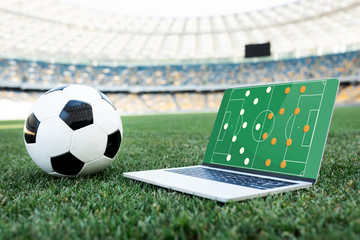 soccer ball and laptop with formation on screen on grassy football pitch at stadium