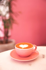 Pink cup of cappuccino on marble table with pink pastel wall on background.