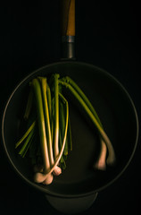 
A few tender garlics of white and green color in a large frying pan on a black background. Vertical format.