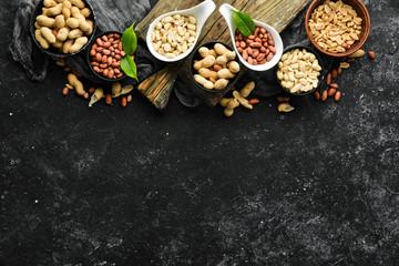 Set of peanuts in bowls on a black stone background. Nut background. Top view.