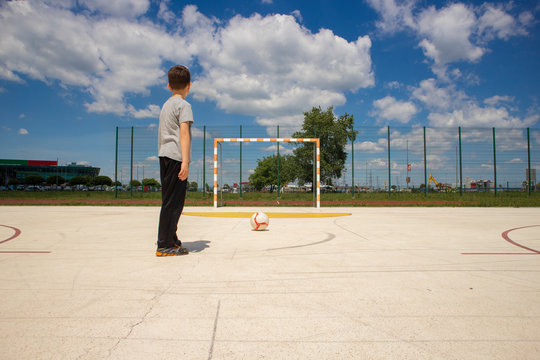 Football loving boy practicing penalty kicks by shooting ball on empty goal