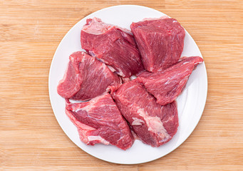 Raw large pieces of beef for bbq or goulash meat on white plate, top view