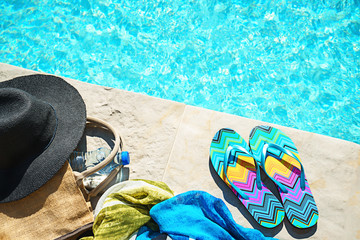 Swimming pool and straw hat, colorful flip flops, wicker bag, straw hat, bottle with still water as...