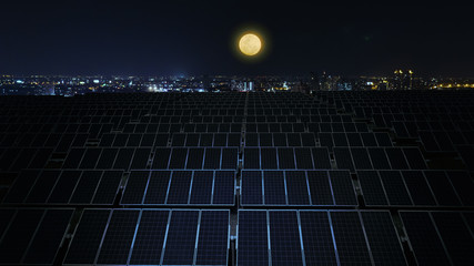 Solar panels at night with full moon and city background.