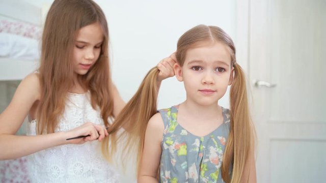 little girl makes ponytails of her younger sister